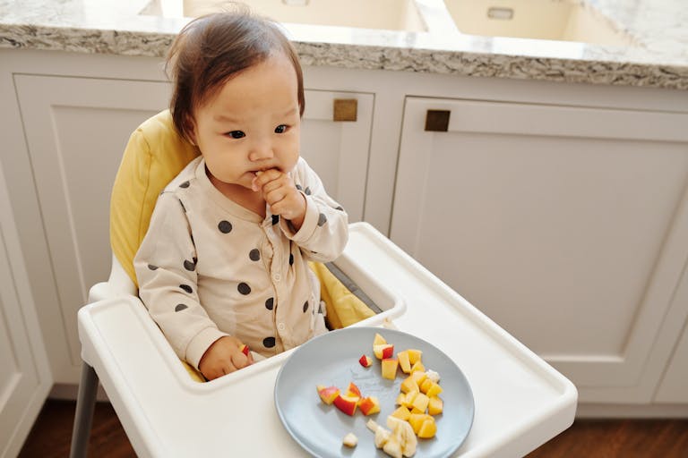 Cute toddler sitting in a high chair enjoying a healthy fruit snack indoors.
